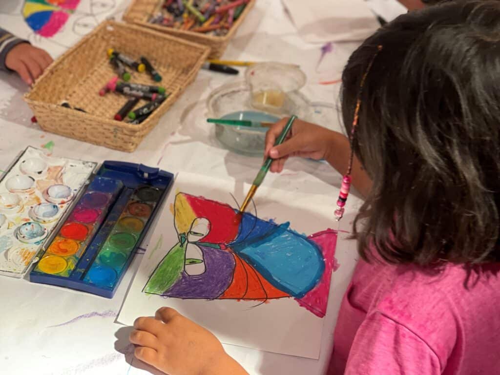 A little girl in a pink shirt painting a colorful picture on a sheet of paper.