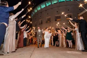A newly married couple walking out of their wedding venue while being celebrated by guests.