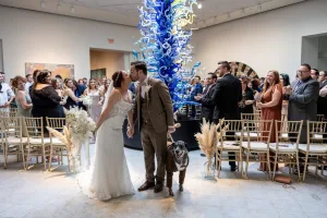 Newlyweds share a kiss in the Council of 101 Grand Gallery wedding venue, celebrating with family, friends, and their dog.