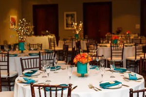 Tables in a meeting room dressed in white cloths with blue and white decorations.