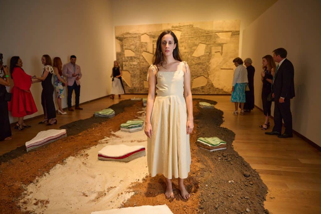 2025 FL Prize artist, Amanda Linares standing in the middle of her installation made of soil, glass, ceramics, and concrete.