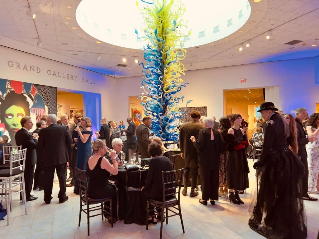 Adults mingling at a formal event in a gallery with a sculpture in the middle of the room.