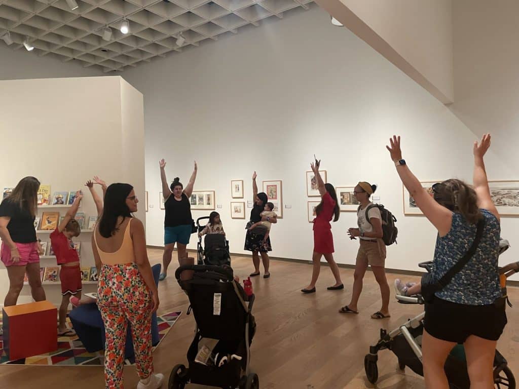 Mothers and children stretching their arms up in a gallery.