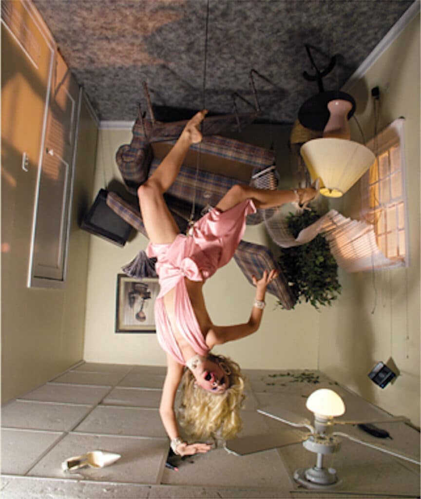 a woman hanging upside-down in a pink dress, mouth open. The scene behind her crashes as it tilts.