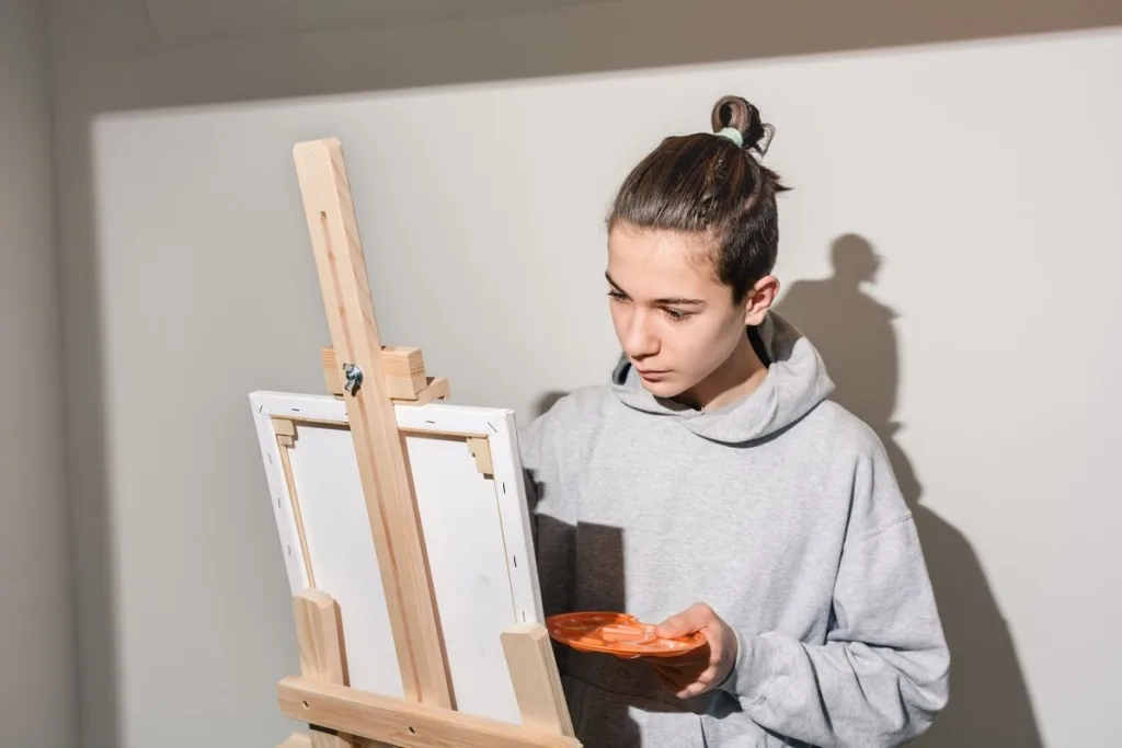 a teenage boy painting on a canvas