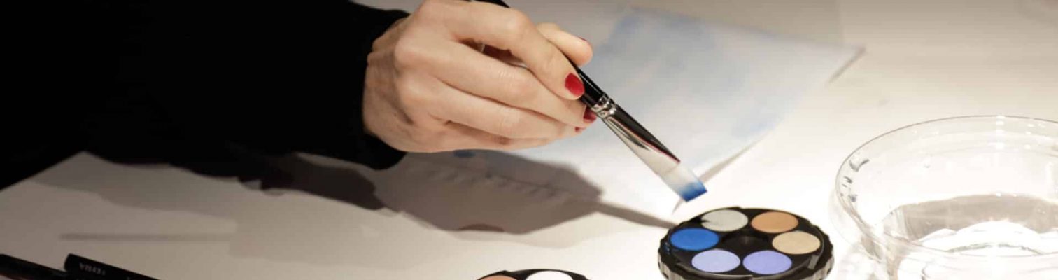 A woman applying blue paint to her brush during an adult art class.