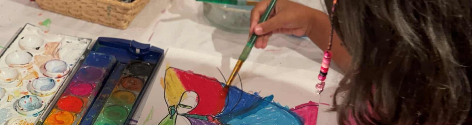 A little girl in a pink shirt painting a colorful picture on a sheet of paper.
